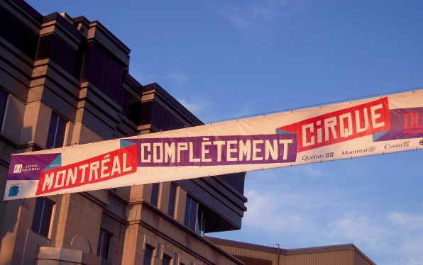 sign for Montréal Complement Cirque in front of blue sky and pink brick building